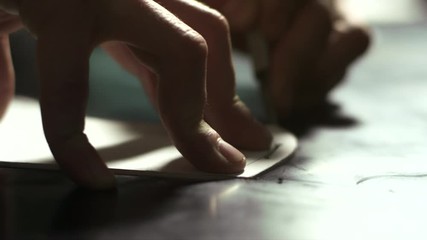 Handmade leather making. Close up leatherworker hands cutting out leather sketch. Leather pattern cutting on table in workshop. Male hands cutting skin with stencil knife. Exclusive manufacturing