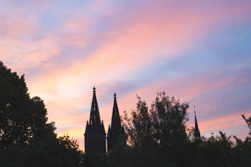 Obraz premium towers Church of St Ludmila Kostel sv. Ludmily in Prague in the distance against the background of the sunset and the pink sky and green forest