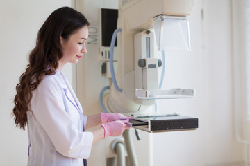 Side view of the young breast specialist in pink gloves who is preparing the apparatus of the ultrasound examination of the breast for carrying up the ultrasound examination in her office