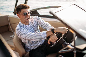 Adult male buyer in classic apparel driving expensive sailing boat, testing her motion and speed in...