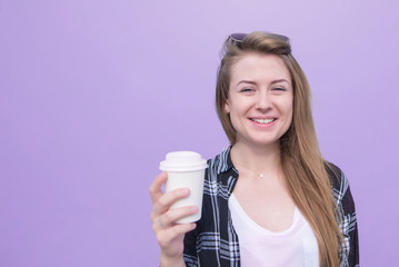 Smiling student girl with a glass of coffee in his hands is isolated on a purple background. happy woman standing with a cup in her hands and looking into the camera on a purple background. Copyspace