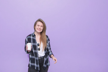 Portrait of an attractive girl standing on a purple background with a paper cup in her hands and...