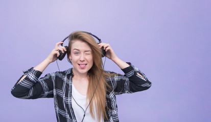 Attractive young girl with headphones is on a purple background and looks at the camera. Funny girl posing with headphones on a purple background. Copyspace