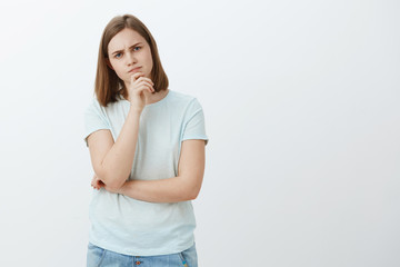 Girl hard to impress. Smart and curious thoughtful attractive caucasian female student holding hand on chin thinking frowning while making impression standing and making decision over grey background