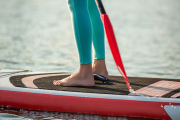 Cropped image of confident woman standing with a paddle on the surfboard, SUP