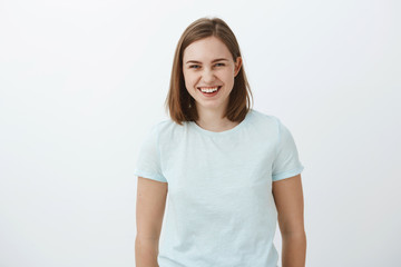 Waist-up shot of joyful entertained and amused good-looking ordinary brunette girl in trendy t-shirt laughing happily and gazing at camera having amusing funny talk with friends over gray background