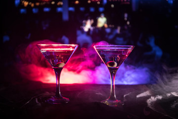 Several glasses of famous cocktail Martini, shot at a bar with dark toned foggy background and disco lights. Club drink concept