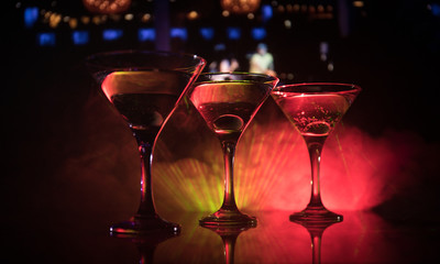 Several glasses of famous cocktail Martini, shot at a bar with dark toned foggy background and disco lights. Club drink concept