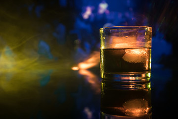 selective focus pure whisky with ice cube inside whisky glass on dark foggy background alcohol drink concept.