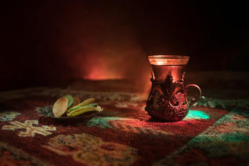 Arabian tea in glass with eastern snacks on a carpet on dark background with lights and smoke....