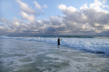 Fototapeta na wymiar Scène de pêche en mer. Pêcheur en surf casting en action entrain de lancer. pêche du bord sur une plage