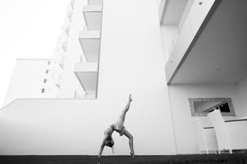 black and white image fine art representing beautiful thin babe female young athlete doing yoga and pilates positions outside home in a garden with all the building in background. line 