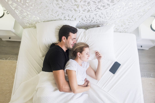 aerial view of beautiful caucasian young beautiful couple sleeping at home in a white bed in the bedroom. stylish home and pretty people resting together with love and protection. happy moning