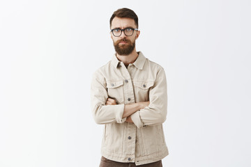 Portrait of dissatisfied intense man hearing shocking unpleasant news frowning crossing hands on chest and pursing lips looking disappointed and upset standing questioned over gray background