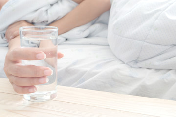 Woman hand a glass of water. While lying . The concept of drinking water and health.