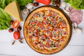 Delicious fresh Pizza with mashrooms, bacon and pepper on the white wooden table surrounded by fresh products