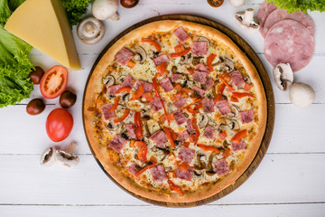 Fototapeta na wymiar Fresh hot pizza surrounded by ingredients on light wooden background