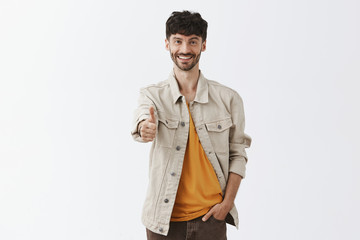 Obraz premium Indoor shot of friendly upbeat and satisfied handsome mature male entrepreneur in trendy outdoor clothes pulling hand towards camera in thumb up gesture smiling replying on excellent idea
