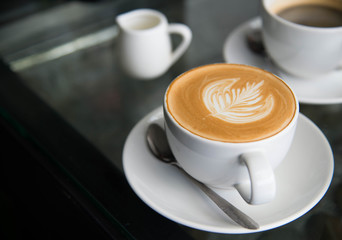 White cup of coffee latte art leave from fresh milk on the table.