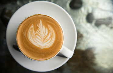 White cup of coffee latte art leave from fresh milk on the table.