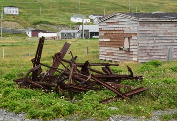 closeup of a bunch of rusty anchors stored on a grass area near an old shack 