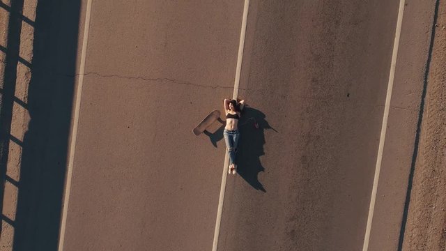 aerial. a girl in ragged jeans and a T-shirt lies on the highway. girl with a skateboard resting. View from above