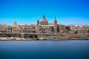 Fototapeta na wymiar Old Valetta cityscape in mediterranean Malta island observed accross the harbour bay with visible cathedral dome