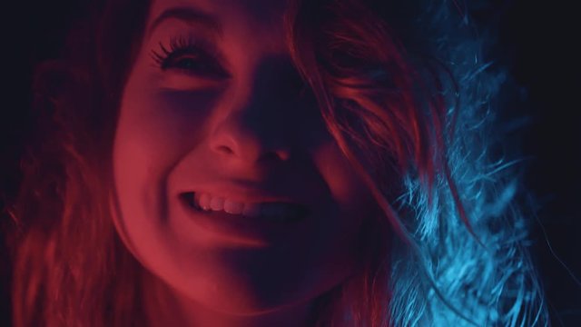 Woman model in studio smiling seductively under vibrant colorful lights