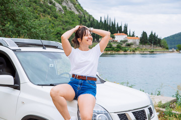 woman sitting at car hood sea and mountains on background