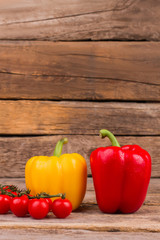 Fresh yellow and red bell peppers. Little ripe cherry tomatoes on wooden background. Still life.