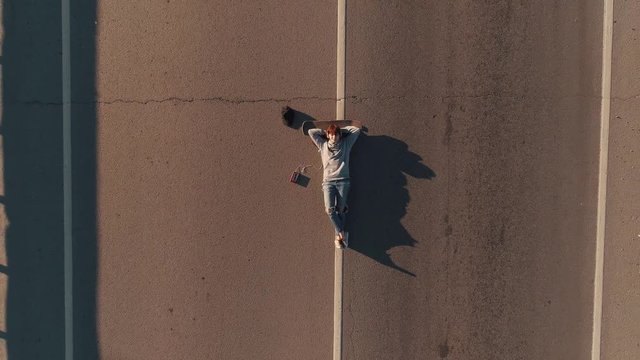 aerial. portrait of a teenage girl from a bird's eye view. A girl skateboarder lies on the roadway and listens to music on headphones