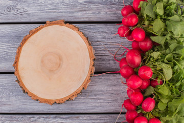 Round wooden board and radishes. Grey wood background.