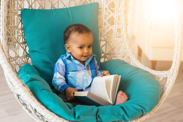 Portrait of African American baby boy holding book on chair.