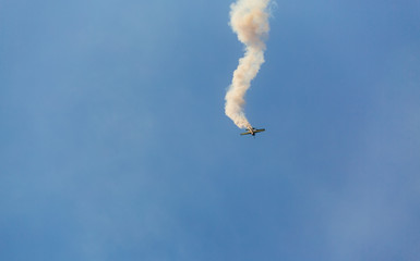 Unidentifiable single airplane performing acrobatic flight on blue sky. Trace of Smoke behind. Falling from the sky