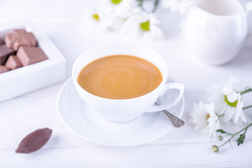 Coffee with milk, chocolate candies and chrysanthemums flowers on a white background