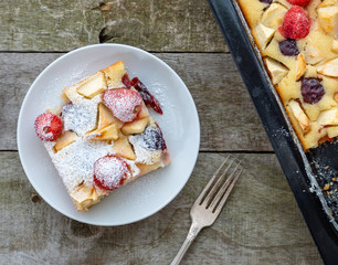 Strawberry plum cake on white plate and natural wooden desk.