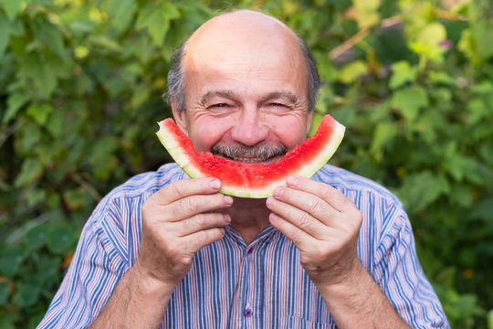 Mature caucasian man with mustache eating juicy water melon with pleasure and smiling.