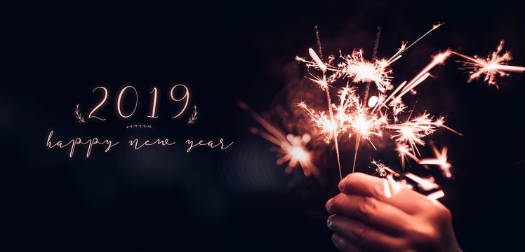 Hand holding burning Sparkler blast with happy new year 2019 on a black bokeh background at night,holiday celebration event party,dark vintage tone.