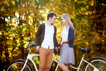 Fototapeta na wymiar Active happy romantic couple, bearded man and attractive woman close together at tandem double bicycle outdoors in autumn park or forest on sunny bright golden yellow trees dense foliage background.