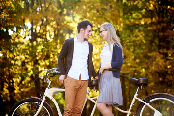 Obraz premium Active happy romantic couple, bearded man and attractive woman close together at tandem double bicycle outdoors in autumn park or forest on sunny bright golden yellow trees dense foliage background.