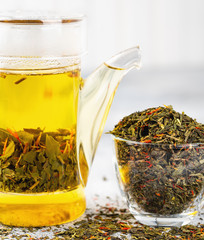 Green tea with strawberry flowers in teapot on gray table on light background