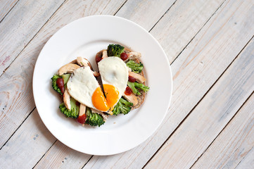 The fried egg in the form of heart with vegetables and bread on a white plate