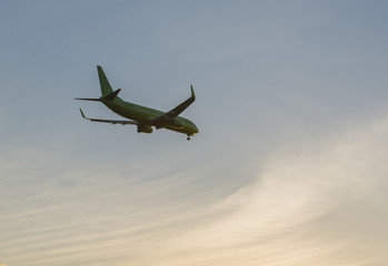 The Plane Flies In The Sky Against The Background Of Clouds
