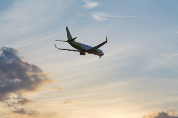 The Plane Flies In The Sky Against The Background Of Clouds
