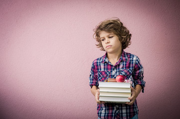 Little boy with stack of books frowning because he has to go back to school.