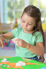 Portrait of a llittle girl is cutting color paper