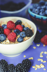 Healthy breakfast. White plate with oatmeal strewn and different berries on a blue background.