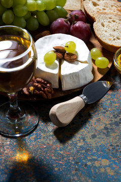 snacks, glass of wine and Camembert cheese on a dark background, vertical, closeup