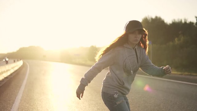 portrait of a red-haired girl skating on a skateboard at sunset. Young attractive girl in headphones, ragged jeans and a sweater in the rays of the setting sun. slow motion