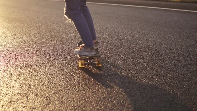 legs girl skateboarding close-up. A girl in sneakers and torn jeans is riding a skateboard along a deserted highway at sunset
